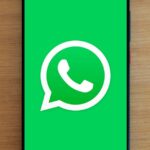 Top view of smartphone displaying WhatsApp logo on a wooden background, representing technology and communication.